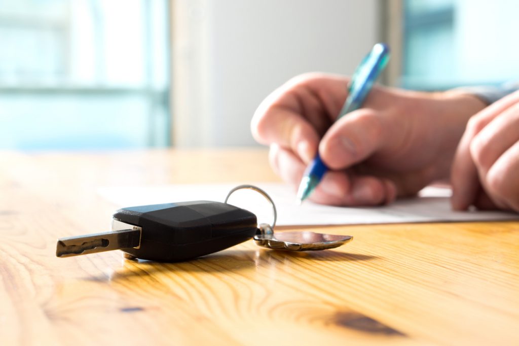 Man signing document with car keys on table.