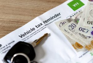 A vehicle tax reminder document of a desk with car keys and money.