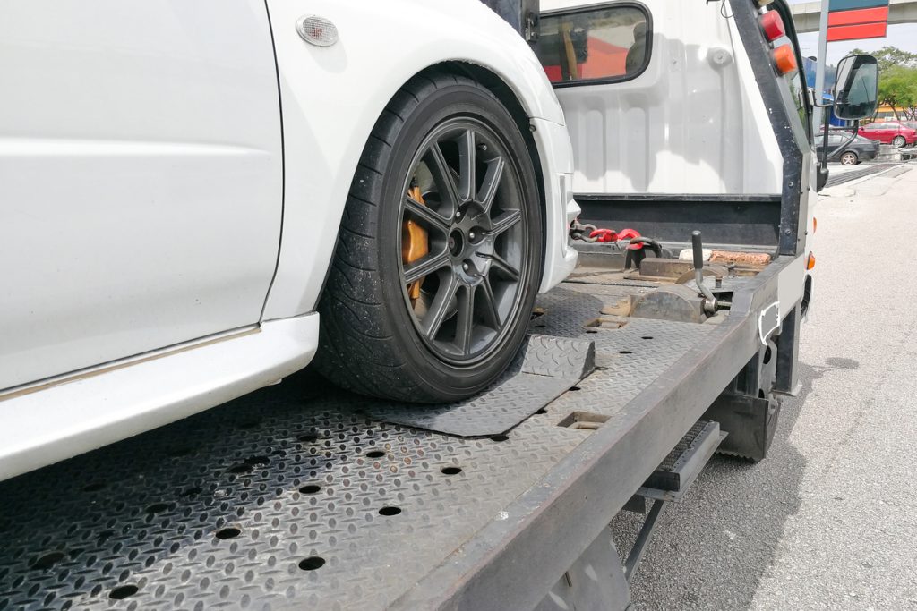 Broken down auto vehicle car towed onto flatbed tow truck with hook and chain